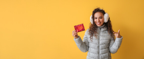 Young woman in winter clothes and with gift card on color background with space for text