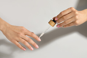 Woman applying oil from pipette to cuticle on light background