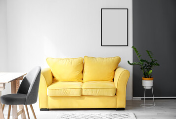 Comfy yellow sofa and blank frame hanging on light wall