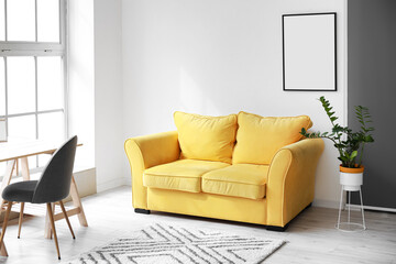 Comfy yellow sofa and blank frame hanging on light wall