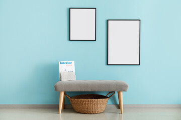 Ottoman with magazine and blank frames hanging on blue wall