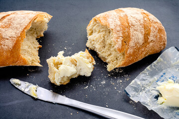 Buttered Piece of Freshly Baked Baguette: French bread with butter on a dark background