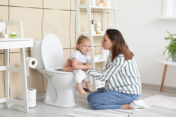 Woman teaching her baby to use toilet bowl in bathroom