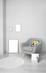 Blank frames and grey armchair near light wall