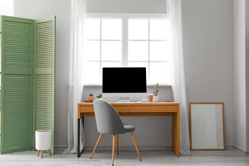 Wooden table with computer, cup of coffee and flowerpots near window in room