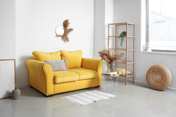 Interior of stylish living room with yellow sofa, shelving unit and dry reeds