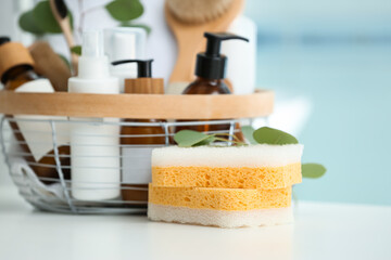 Bath sponges and basket with bottles of cosmetic products on white table