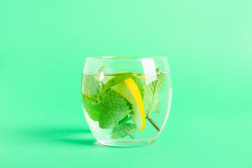 Glass of water with mint and lemon on color background