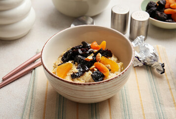 Sweet oatmeal with prunes, dried apricots and almond nuts in bowl on light table
