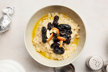Sweet oatmeal with prunes and almond nuts in bowl on light table