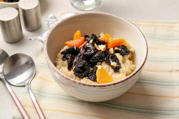 Tasty sweet oatmeal with prunes, dried apricots and almond nuts in bowl on light table