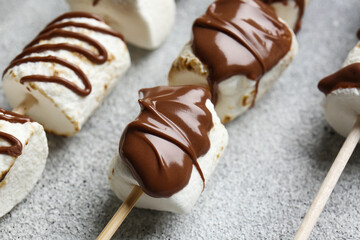 Skewers with tasty grilled marshmallows in chocolate on light background, closeup