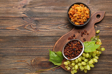 Bowls with tasty raisins and ripe grapes on wooden background