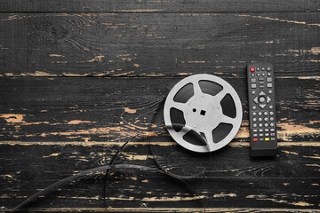 Modern TV remote control and film reel on dark wooden background