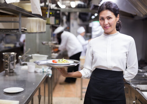 positive female waitstaff standing with tray in kitchen in restaurante