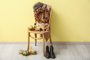Beautiful acorn wreath with books on chair, pumpkins, boots and candles near yellow wall