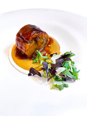 delicious gourmet dish of oxtail in sauce with salad, stewed meat with honey sauce, served on a white plate, vertical