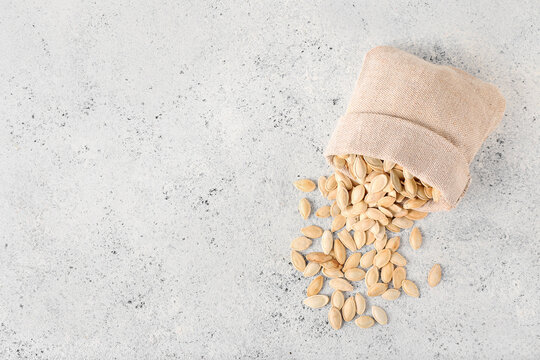 Bag with natural pumpkin seeds on light background