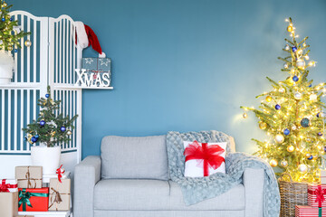 Grey sofa with Christmas trees and folding screen near blue wall