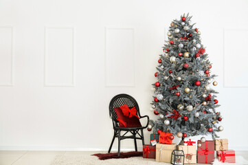 Beautiful Christmas tree, gift boxes and chair near white wall