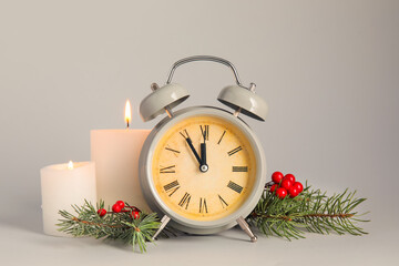 Alarm clock, fir branches and burning candles on grey background