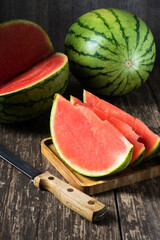 One whole watermelon with sliced pieces and a knife on a wooden background.