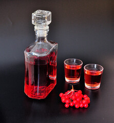 Viburnum liqueur, strong homemade alcohol in a glass decanter and two glasses with a bunch of ripe...
