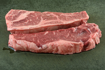 Fresh raw New York strip steaks on black cutting board