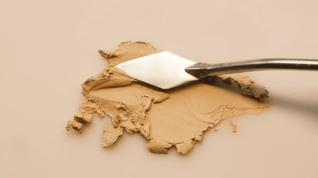 Smearing foundation cream on beige background, sample tone texture close-up. Makeup and beauty products concept, cosmetics, eyeshadow palette, bronzer or concealer.