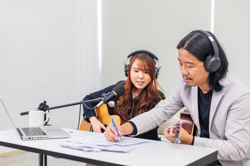 Asian duo rock band is composing song as the male member is writing lyrics on paper while working...