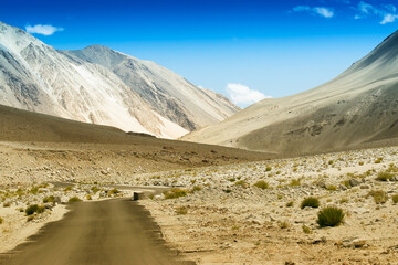 A concrete road towards beautiful rocky mountains and blue sky with peaks of Himalaya, Leh, Ladakh, Jammu and Kashmir, India