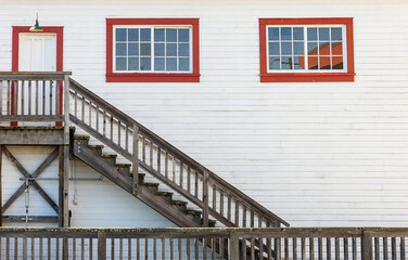 Wooden white house entrance with red windows and door with rustic wooden staircase in British Columbia
