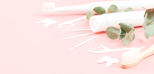 Bamboo toothbrush, floss, toothpicks and a tube of toothpaste on the right on a soft pink