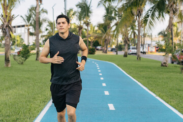 Front view of a hispanic young adult man running at a public park in the morning copy space