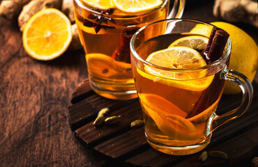 Hot black winter tea with ginger, honey, lemon and spice. Immune booster drink in glass cup on rustic wooden table background, copy space