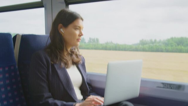 Businesswoman with earbuds listening to music commuting to work on train working on laptop - shot in slow motion