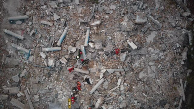 Zoom in aerial view of rescuers and paramedics walking on concrete rubble of destroyed building after natural disaster