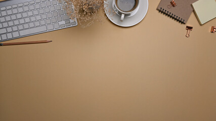 Top view minimal workspace with keyboard, coffee cup and notebook on beige background.