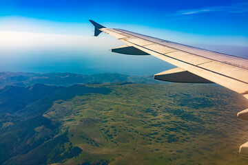 Fototapeta na wymiar View of airplane wing, blue skies and green land during landing. Airplane window view.