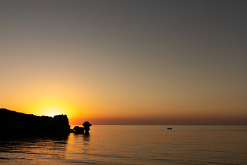 Sunset on the sea, rocks and sun, silhouette and boat with fishermen. Sea of Azov, Russia.