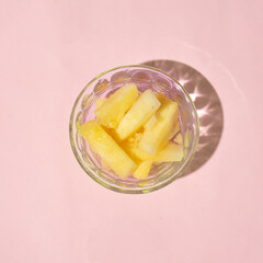 Pineapple cut inside a glass container on a pink background