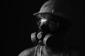 Portrait miner in helmet, respirator and goggles looking at light.Dirty worker in black and white...