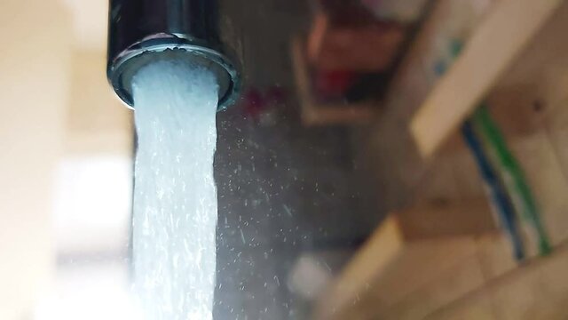 Water from the tap flows in slow motion. Water cost and tariffs, water saving, close-up. Background