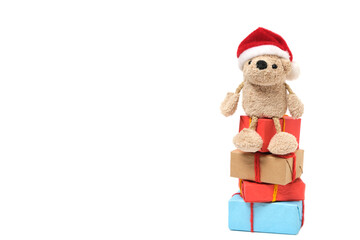 Small teddy bear in a Santa Claus hat sits on boxes with Christmas gifts.On a white background.