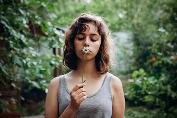 Teenager Girl sniffing chamomile flower in the forest. Natural beauty. Candid moments - obrazy, fototapety, plakaty