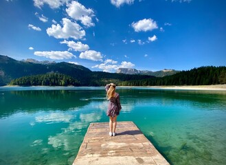 An amazing lake and blue sky, a little bridge and a blond girl standing on it. Concept of solitude, relaxing, amazing nature and human. 