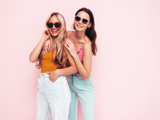 Two young beautiful smiling brunette hipster female in trendy summer clothes. Sexy carefree women posing near pink wall. Positive models having fun. Cheerful and happy. In sunglasses