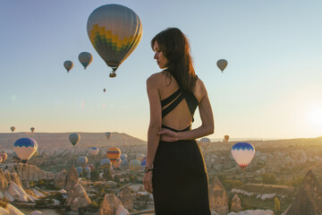Woman watching the sunrise and hot air balloons taking off over valley in Cappadocia, Goreme, Turkey