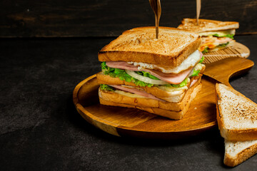 Homemade club sandwich with ham, egg and cheese,tomatoe, lettuce,onion on dark background. Rustic style. Selective Focus. Copy space. No.02