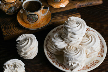 Marshmallow on a plate and coffee in a vintage cup on a dark wooden table, background with copy space
